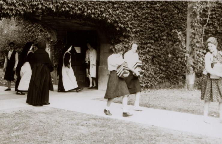 CSJ sisters and students carrying books  under the archway by  the chapel